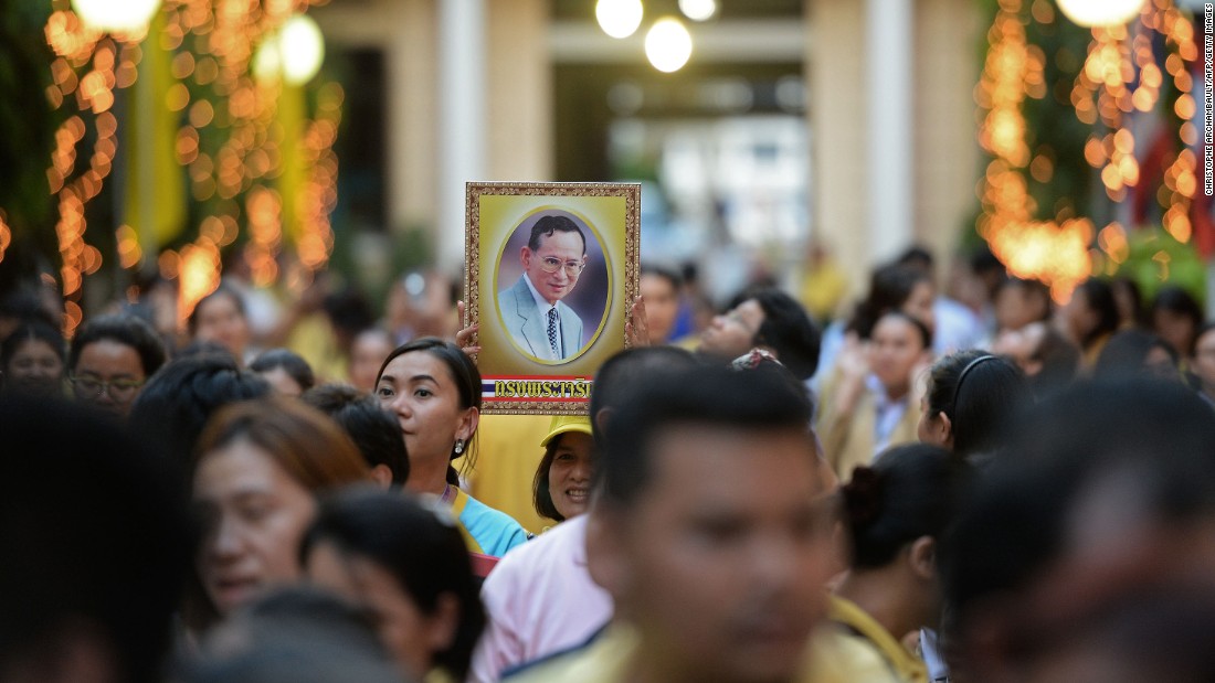 A portrait of the King is held on the eve of his 88th birthday as people gather outside the Siriraj hospital in 2015. The King of Thailand is regarded as a demi-god by many Thais, and his popularity has been viewed as a unifying force during times of political unrest.