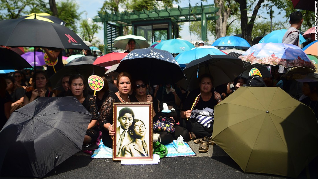 Mourners shade themselves under umbrellas while they await the procession of the King&#39;s body to the palace in Bangkok on October 14. 