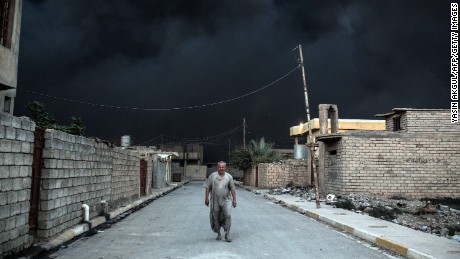 An Iraqi man escapes the thick black smoke of an oil field set on fire in Qayyarah