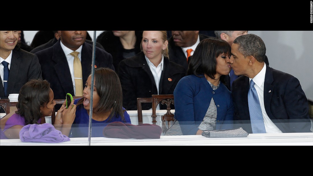 Obama kisses his wife during the inaugural parade in Washington. Sasha, left, takes a photo of her sister, Malia.