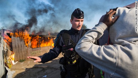 A police officer stands guard after migrants burn down a shelter as authorities move in to clear the camp on Tuesday.