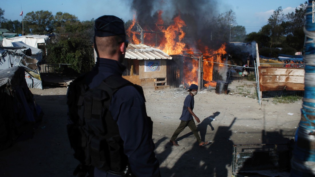 A man passes a camp structure on fire on October 25.