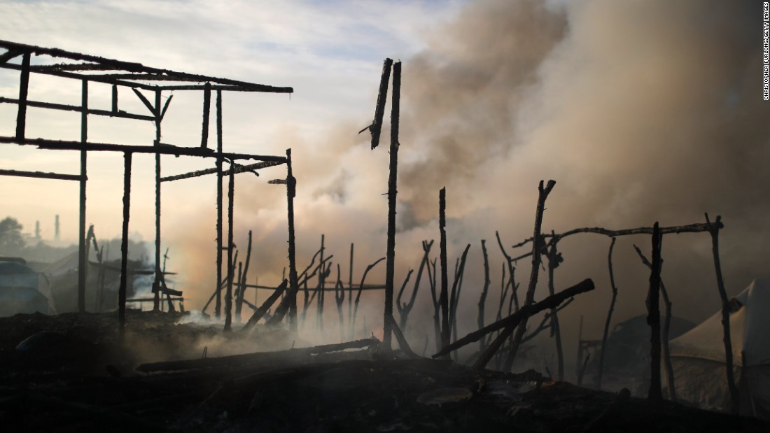 The remains of makeshift structures smolder from fires that broke out overnight in parts of the camp on October 26.