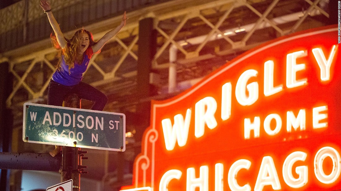 A Chicago fan straddles a street pole outside Wrigley Field as people gather to celebrate the Cubs&#39; dramatic win. 