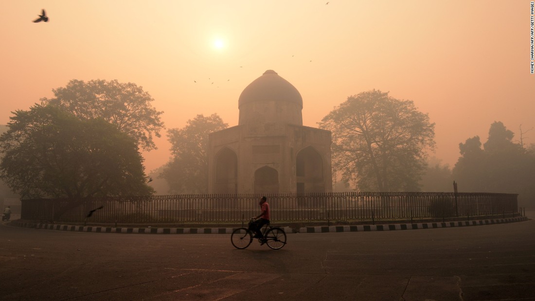 An Indian cyclist rides along a street as smog envelops a monument in New Delhi on October 31, the day after the Diwali festival.