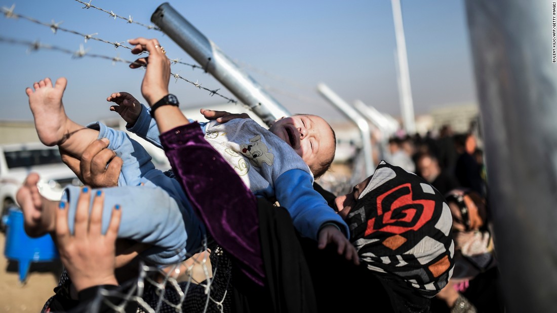 A baby is passed through a fence back to his mother at a refugee camp in the Khazir region on Saturday, November 5.