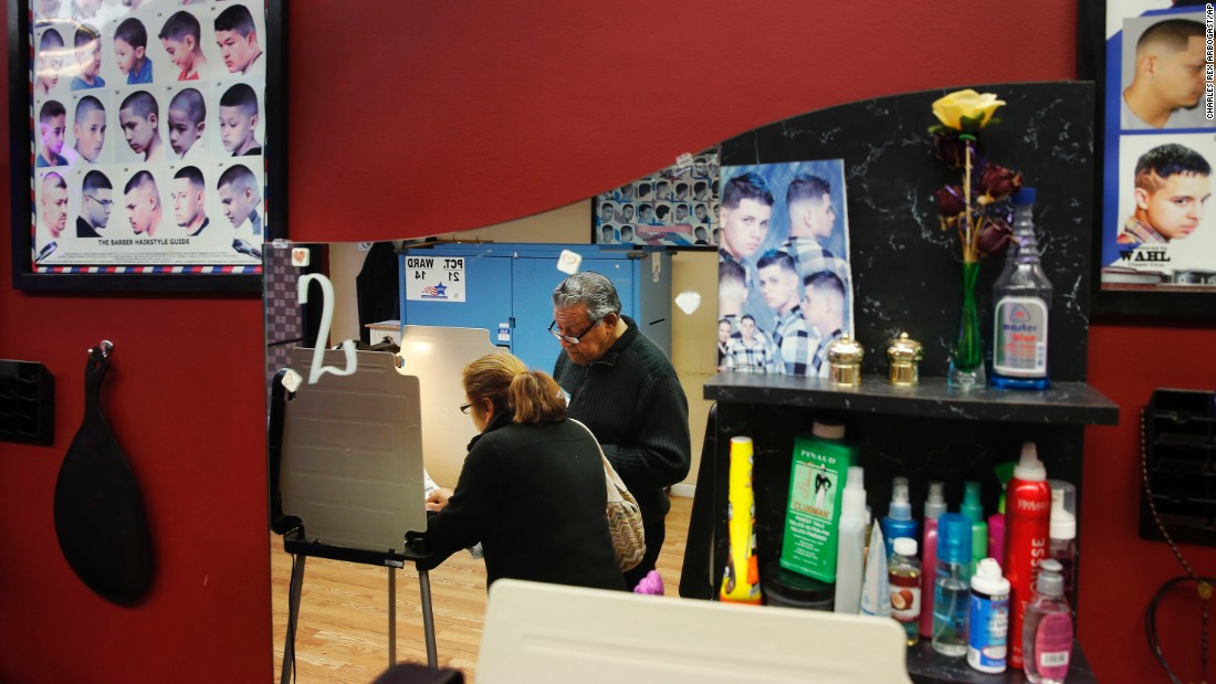 Democratic polling judge John Ramirez is reflected in a mirror as he helps a voter at a beauty salon in Chicago.