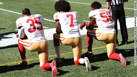 Quarterback Colin Kaepernick (center) with teammates Eric Reid (L) and Eli Harold #58 of the San Francisco 49ers kneel on the sidelines during the national anthem before the game against the Seattle Seahawks on September 25, 2016 in Seattle.