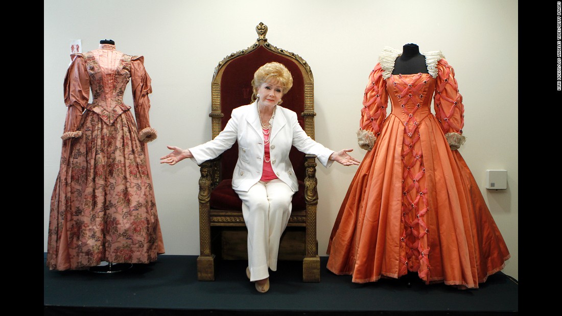 Reynolds poses before the auction of her massive collection of memorabilia from classic movies in 2011. Reynolds is siting on the throne from the 1955 movie &quot;Virgin Queen&quot; with a dress worn by Bette Davis, right,  and Joan Collins, left.