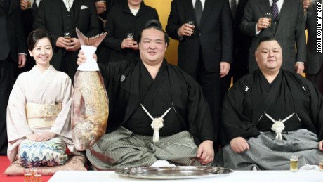 Kisenosato holds a fish during a ceremony promoting him to the highest rank of sumo wrestling, accompanied by his trainer and trainer&#39;s wife. 