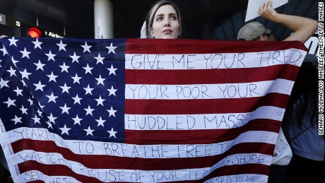 Chella, from Sherman Oaks, holds the U.S. flag with words from the sonnet, &quot;The New Colossus,&quot; by poet Emma Lazarus  while joining people who continue to protest President Donald Trump&#39;s travel ban at the Tom Bradley International Terminal at LAX on January 29, 2017 in Los Angeles, California. 