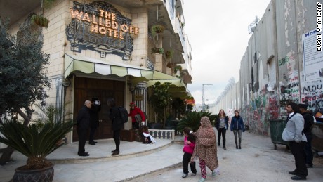 People pass by the "The Walled Off Hotel" and the Israeli security barrier in the West Bank city of Bethlehem, Friday, March 3, 2017. The owner of a guest house packed with the elusive artist Banksy's work has opened the doors of his West Bank establishments to media, showcasing its unique "worst view in the world." The nine-room hotel named "The Walled Off Hotel" will officially open on March 11. (AP Photo/Dusan Vranic)