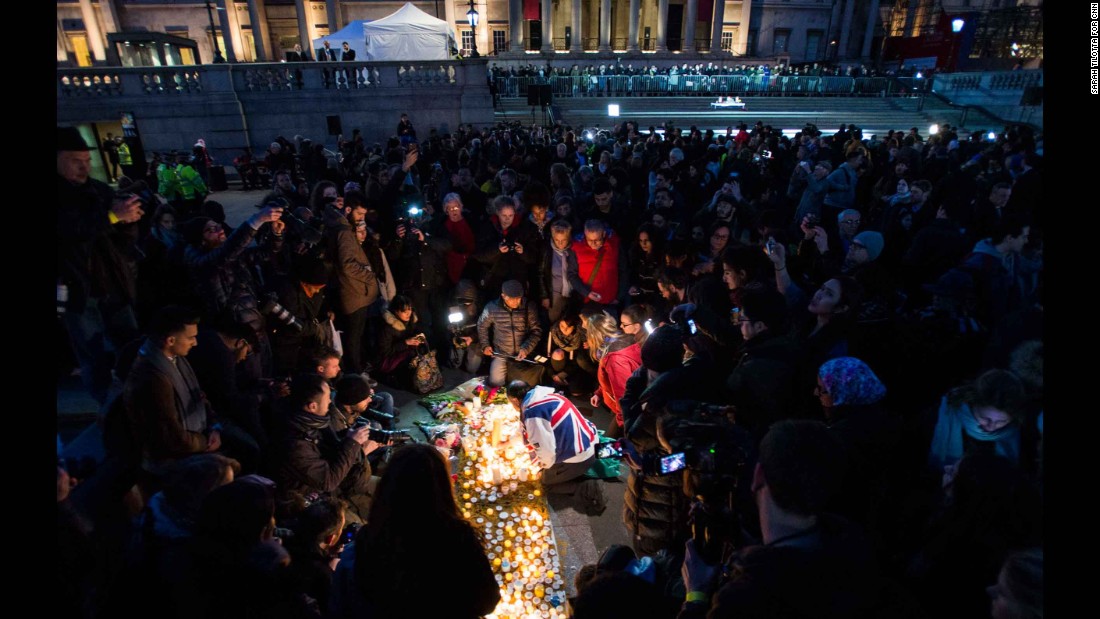 The crowd huddles around 62-year-old John Loughrey (center, draped in Union Jack flag) as he lights candles in tribute to the victims.