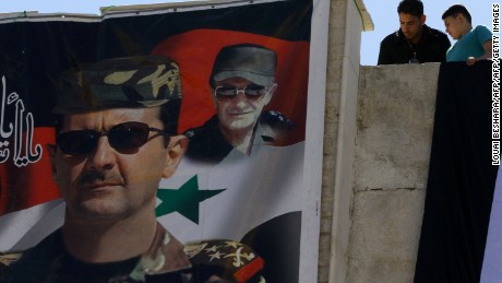 Syrians look down at a poster of Syrian President Bashar al-Assad (L) and his late father and predecessor Hafez al-Assad in Damascus, as they watch the tourist train pass following the re-opening ceremony of the rail route between two neighbourhoods in the Syrian capital, Raboeh and Dumar, on May 1, 2015. AFP PHOTO / LOUAI BESHARA        (Photo credit should read LOUAI BESHARA/AFP/Getty Images)