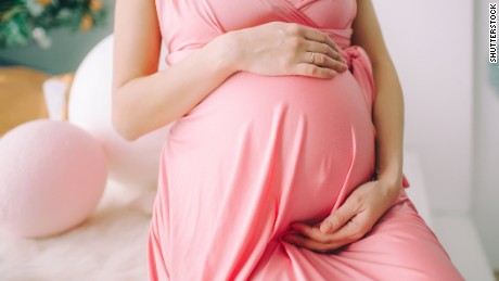 Encantador barriga (barriga) que a mulher grávida em um vestido coral abraça