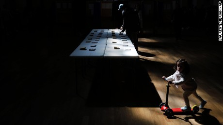 A girl rides a scooter as a man picks up ballots for the first round of the French presidential election in Lyon, France, Sunday April 23, 2017. 