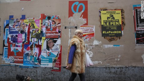 A woman walks past election campaign posters in Paris&#39; 18th district. One poster, in yellow, encourages voters to vote against Marine Le Pen. 