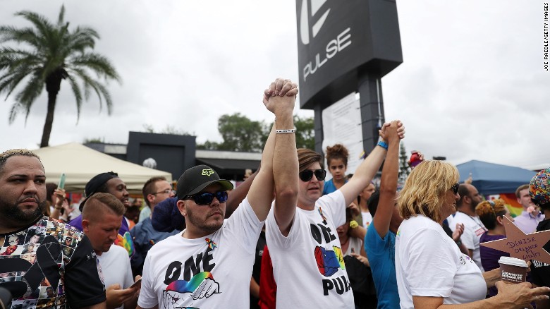 People hold hands Monday, June 12, as they attend a memorial service at the Pulse nightclub in Orlando. A vigil was held at the club a year after a mass shooting <a href=