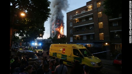 A security cordon holds people back as Grenfell Tower burns.