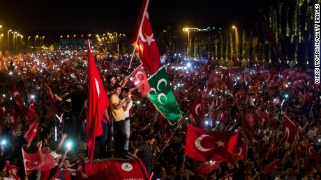ISTANBUL, TURKEY - JULY 15:  People watch on and wave flags as they listen to Turkey&#39;s President Recep Tayyip Erdogan during his speech at the July 15 Martyrs Bridge on the first anniversary of the  July 15, 2016 failed coup attempt on July 15, 2017 in Istanbul, Turkey. People gathered in public squares and at ceremonies across Turkey to mark the first anniversary of the failed coup attempt which saw 249 people die when military personnel attempted to overthrow the government and President Recep Tayyip Erdogan on the night of July 15, 2016.  (Photo by Chris McGrath/Getty Images)