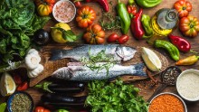 Raw uncooked seabass fish with vegetables, grains, herbs and spices on chopping board over rustic wooden background, top view; Shutterstock ID 415721434