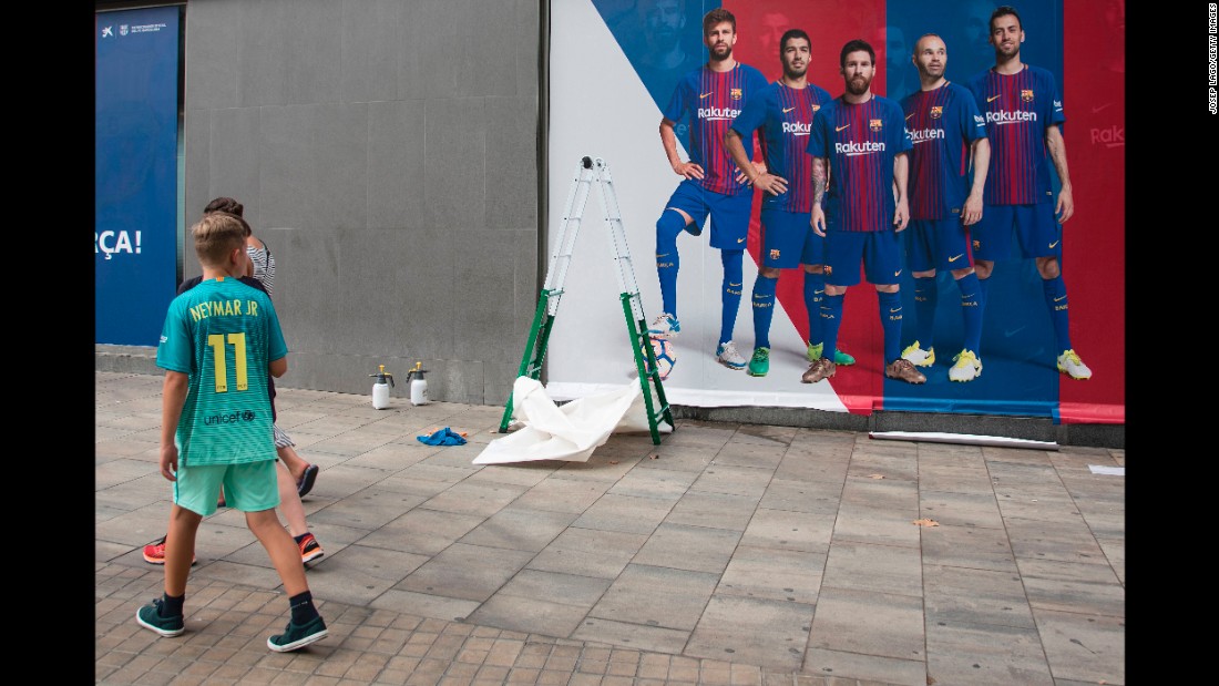 A boy wearing Neymar&#39;s jersey walks past a new Barcelona poster -- without Neymar -- as it is put up outside the Camp Nou stadium on Wednesday, August 2.