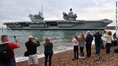 People line the shore to watch as tug boats maneuver the 65,000-ton British aircraft carrier HMS Queen Elizabeth into Portsmouth Harbour.