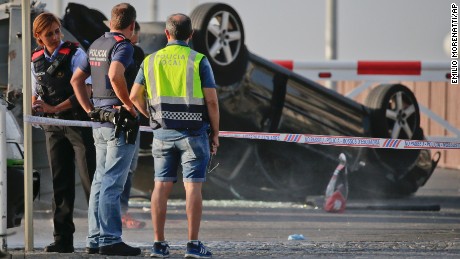 Police officers stand near an overturned car onto a platform at the spot where terrorists were intercepted by police in Cambrils, Friday, Aug. 18.