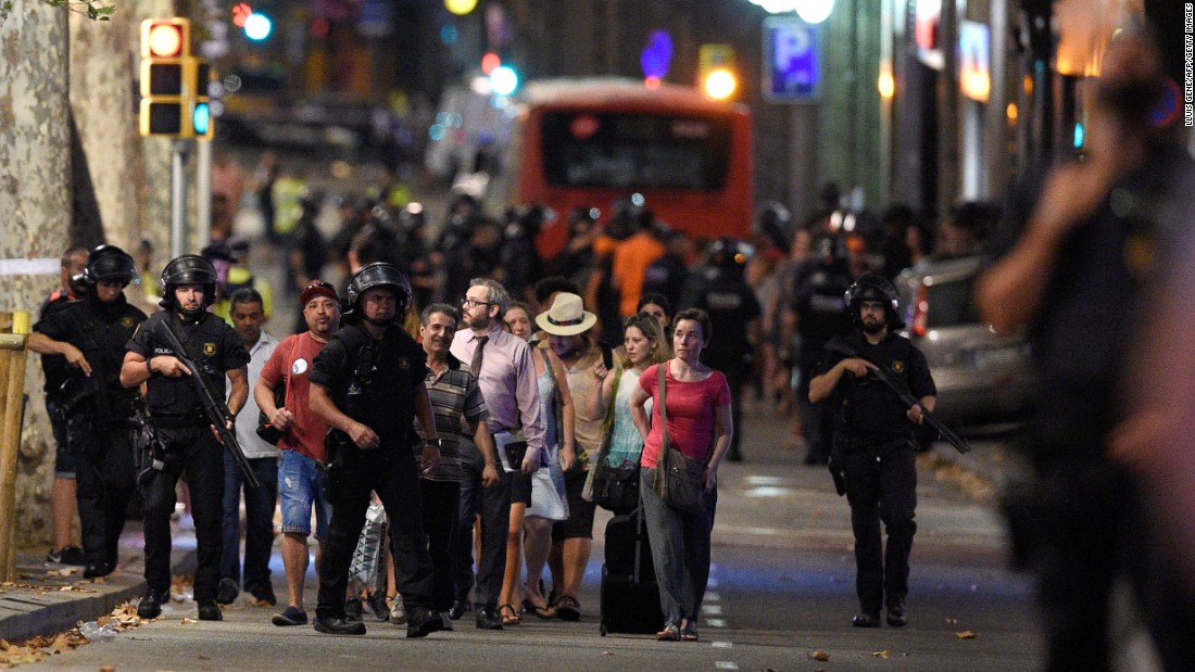 Police accompany clients of a store outside a cordoned off-area of Barcelona. Las Ramblas is especially crowded in the summer, the height of tourist season. The promenade passes by kiosks, flower sellers, cafes and bars.