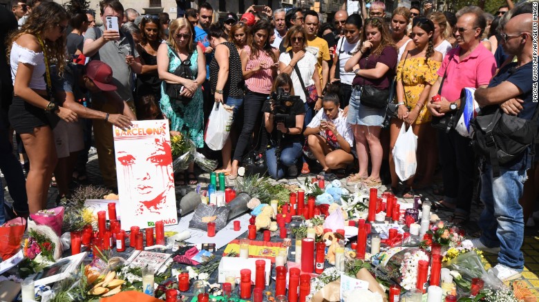 People stand next to flowers, candles and other items set up on the Las Ramblas boulevard in Barcelona as they pay tribute to the victims of the Barcelona attack, a day after a van ploughed into the crowd, killing 13 persons and injuring over 100 on August 18, 2017. 
Police hunted for the driver who rammed a van into pedestrians on an avenue crowded with tourists in Barcelona, leaving 13 people dead and  more than 100 injured, just hours before a second assault in a resort along the coast. / AFP PHOTO / PASCAL GUYOT        (Photo credit should read PASCAL GUYOT/AFP/Getty Images)