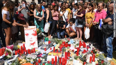 People stand next to flowers, candles and other items set up on the Las Ramblas boulevard in Barcelona as they pay tribute to the victims of the Barcelona attack, a day after a van ploughed into the crowd, killing 13 persons and injuring over 100 on August 18, 2017. 
Police hunted for the driver who rammed a van into pedestrians on an avenue crowded with tourists in Barcelona, leaving 13 people dead and  more than 100 injured, just hours before a second assault in a resort along the coast. / AFP PHOTO / PASCAL GUYOT        (Photo credit should read PASCAL GUYOT/AFP/Getty Images)