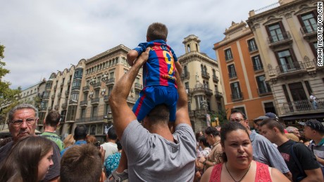 A man hoists a boy in a Barcelona football jersey above a large crowd gathered at the spot where the attacker stopped his deadly rampage.