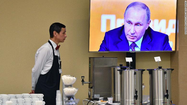 A waiter stands by a screen broadcasting Putin&#39;s marathon annual press conference in Moscow on Thursday.