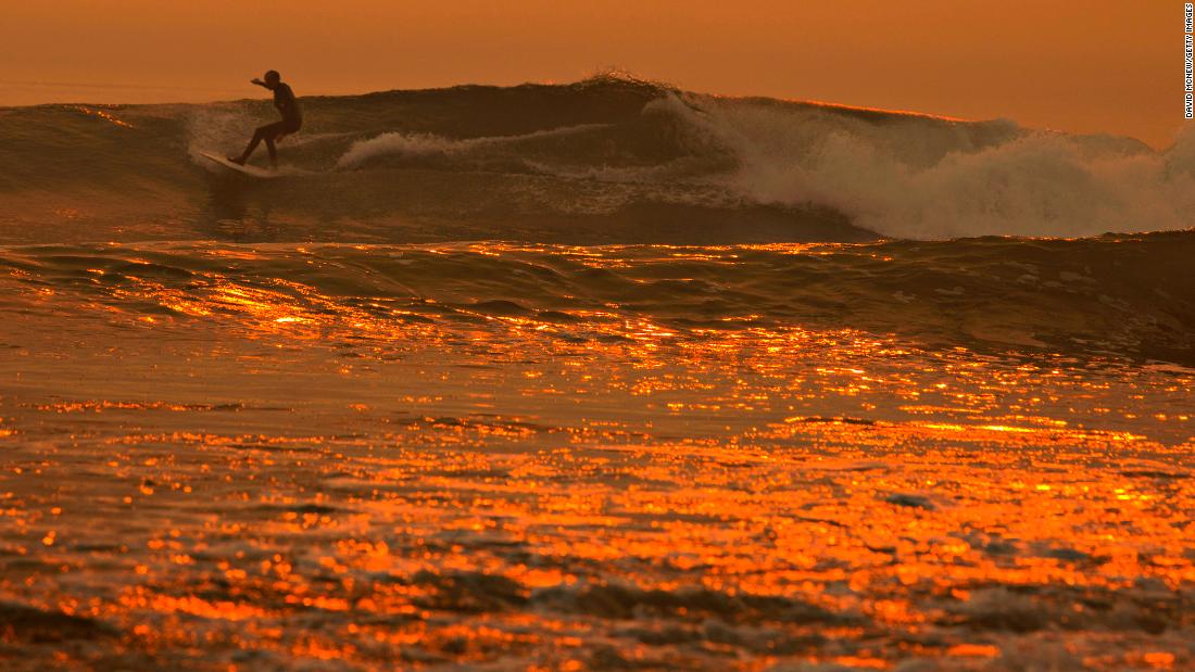 A smoke-filled sky filters sunlight to orange around a surfer as the Thomas Fire continues to grow and threaten communities from Carpinteria to Santa Barbara on Tuesday, December 12, in Carpinteria, California.