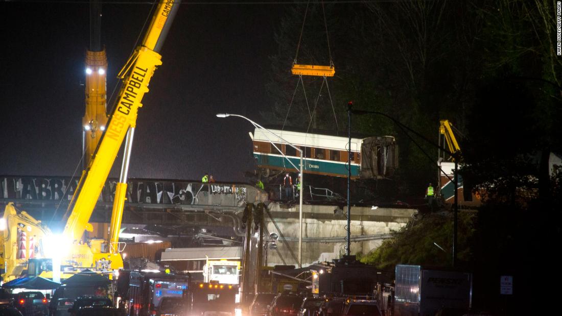 A train car is lifted away on Tuesday, December 19, the day after an Amtrak passenger train derailed near DuPont, Washington. Several of the train&#39;s cars spilled off an overpass and onto Interstate 5.