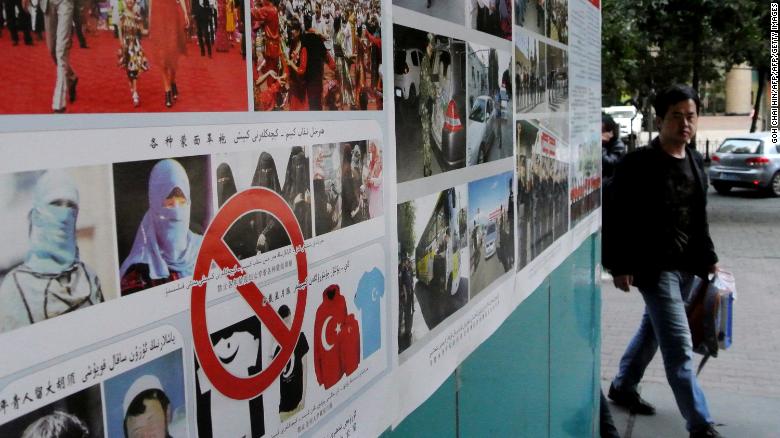 Pedestrians walk past anti-terror propaganda posters pasted along the streets of Urumqi, September 2014.