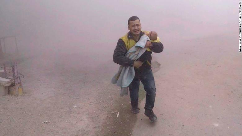 A photo provided by the Syrian Civil Defense group shows what it says is one of its paramedics fleeing with his wounded son from the scene of an airstrike near Damascus on Tuesday.