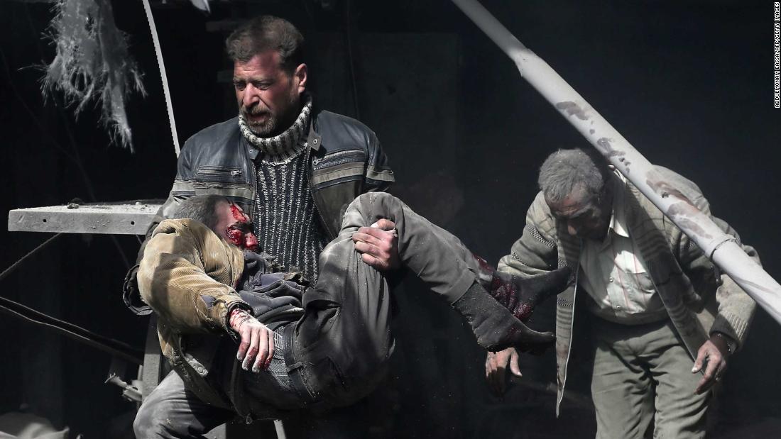 A man carries an injured victim amid the rubble of buildings.