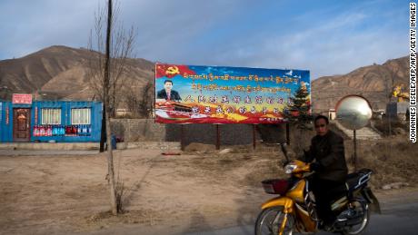 A motorcyclist rides past a propaganda poster showing China&#39;s President Xi Jinping next to a freeway outside of Tongren, Qinghai province on March 2, 2018.