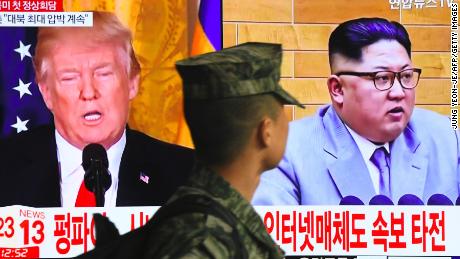 TOPSHOT - A South Korean soldier walks past a television screen showing pictures of US President Donald Trump (L) and North Korean leader Kim Jong Un at a railway station in Seoul on March 9, 2018. 