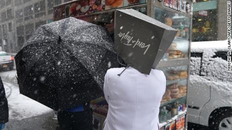 A Lord &amp; Taylor employee takes cover from snow Wednesday on Fifth Avenue in New York. 