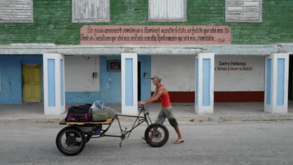 A Cuban man wheels his possessions in Gibara, Cuba, under a sign quoting Fidel Castro:  "A new dawn shall begin to illuminate our future, a future that shall be more brilliant, a Socialism that shall be more refined, a Revolutionary work that will be more promising."