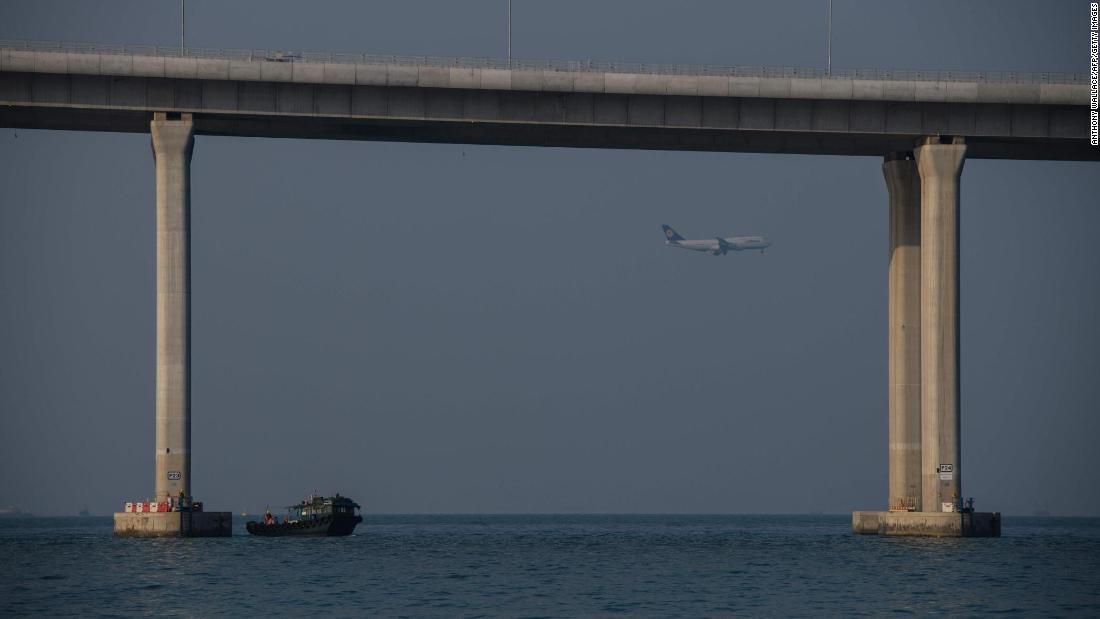 A boat transporting construction workers&#39; berths next to a column of the Hong Kong-Zhuhai-Macau Bridge as a plane prepares to land at Hong Kong&#39;s international airport. 