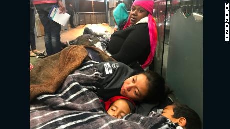 Migrants Tesla Rich, sitting, and Gabriela Hernandez, with sons Jonathan and Omar, try to keep warm as they await border officials to call them for asylum processing. 