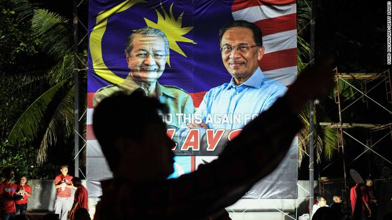 A supporter takes pictures in front of a banner showing former Malaysian Prime Minister Mahathir Mohamad  and Anwar Ibrahim during a rally before the election. 