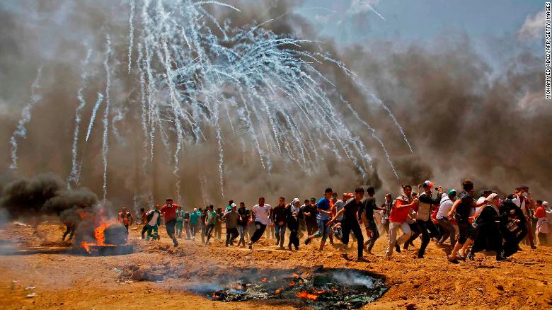  Palestinians run for cover from tear gas on May 14, 2018, during clashes with Israeli security forces near the frontier between Israel and Gaza.