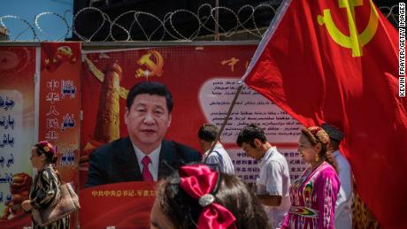 Los miembros de la etnia uigur del Partido Comunista de China llevan una bandera junto a una valla publicitaria del presidente chino Xi Jinping mientras participan en una gira organizada por el casco antiguo de Kashgar, Xinjiang, el 30 de junio de 2017.