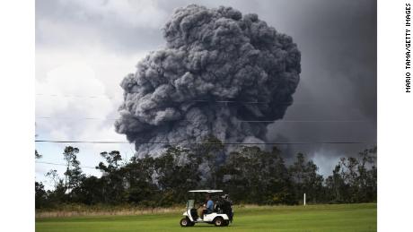 A man drives a golf cart at a golf course as an ash plume rises in the distance from the Kilauea volcano on Hawaii&#39;s Big Island 