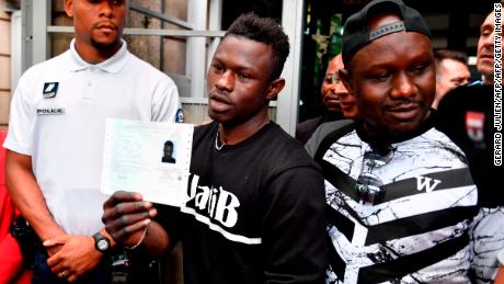 Flanked by his older brother, Gassama holds his temporary residence permit after receiving it Tuesday.