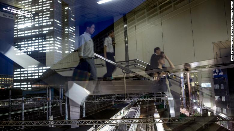 Japanese office workers are seen reflected in a window as they walk to a train station. 